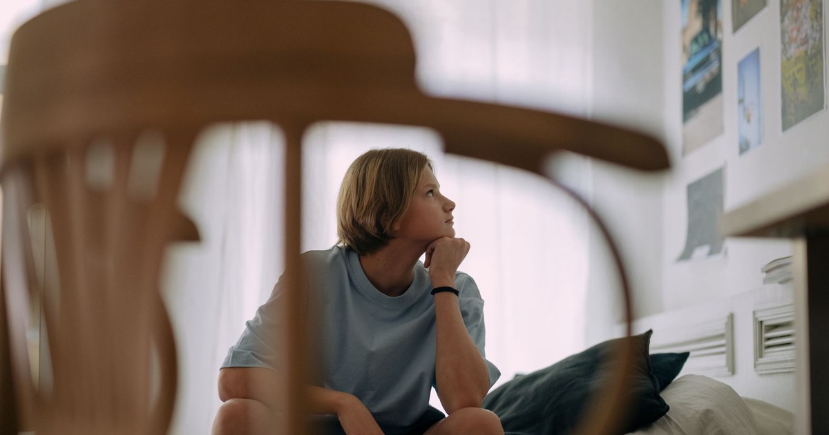 Teenager sitting quietly by a window, looking thoughtful