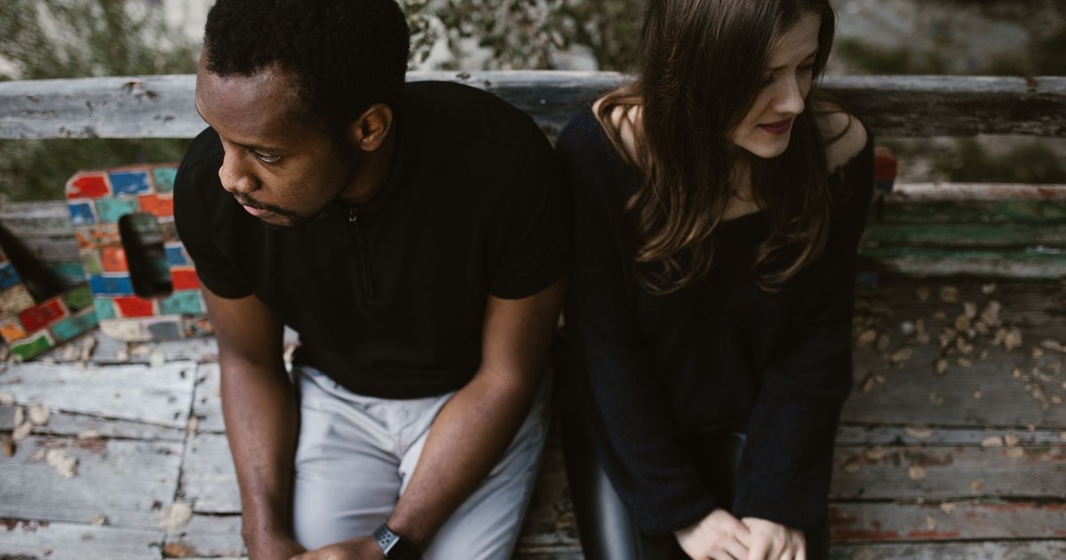 Two people sitting slightly apart on a bench, one looking away