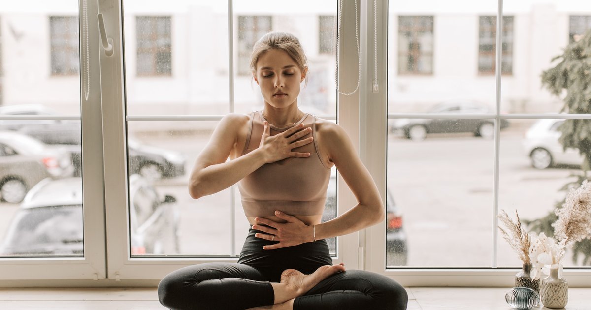 A woman practising slow, grounding breathing by a bright window
