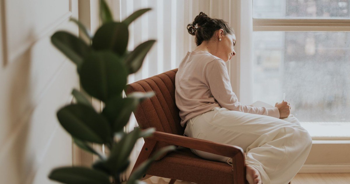 A woman journaling alone by a window, reflecting on her relationship patterns