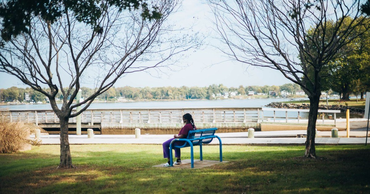 Person sitting alone on a bench by the water, looking calm and reflective
