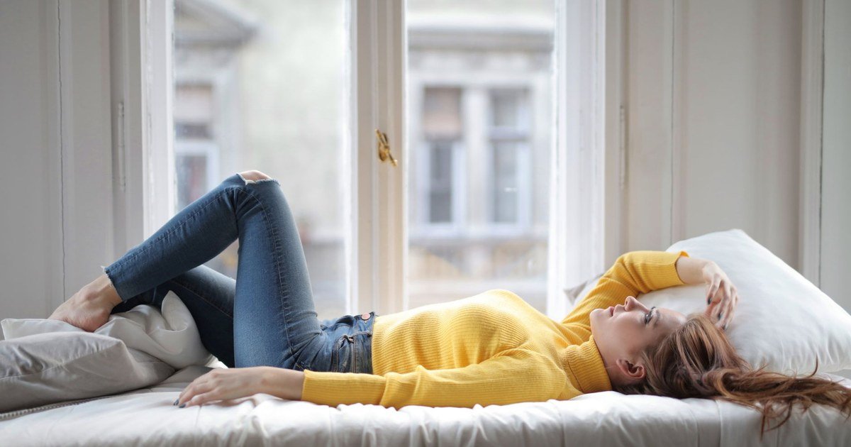 Woman resting on a bed near a bright window, taking a quiet break