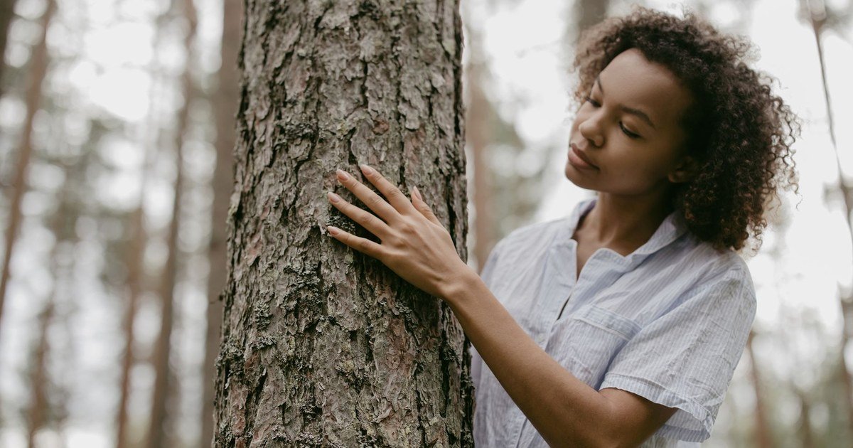 A woman grounding herself by touching a tree during a walk outdoors