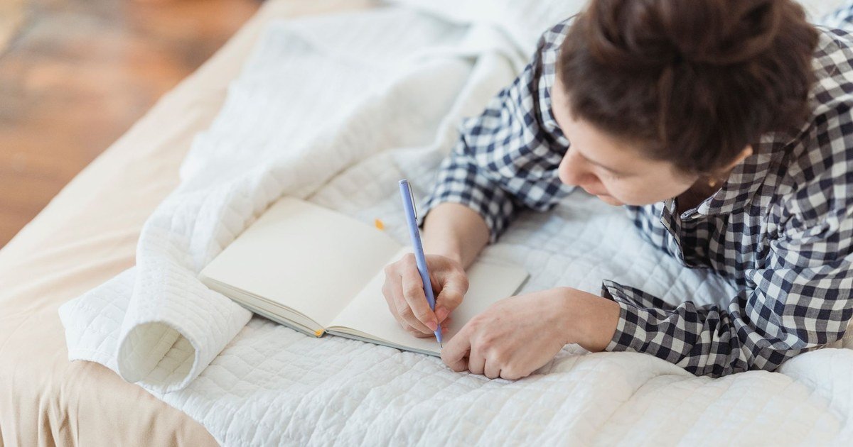 Woman writing in a journal on a cozy bed, naming her emotions