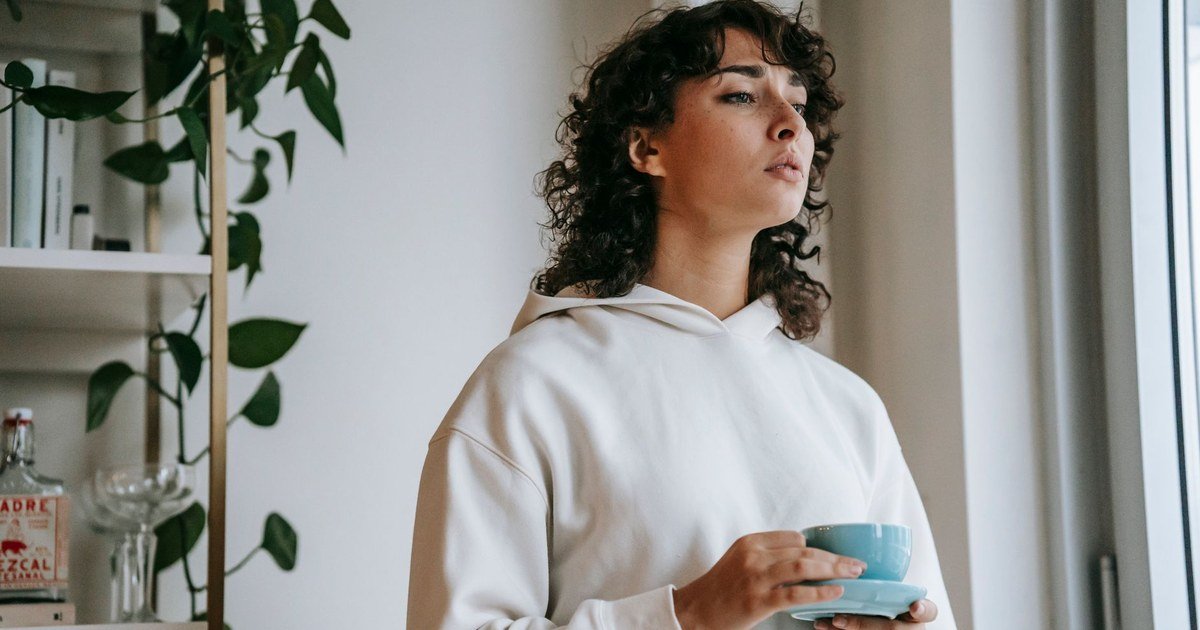 Young woman holding a warm mug, pausing to reflect in a bright room